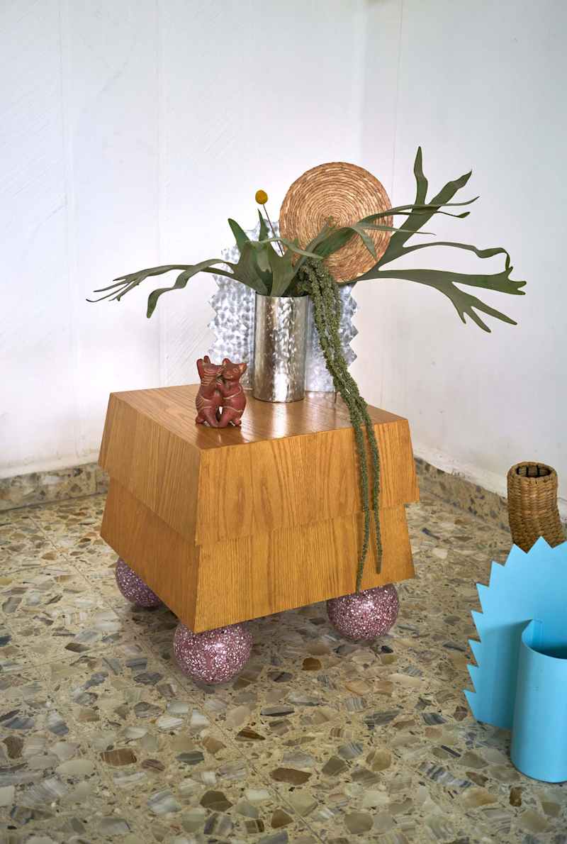 Wooden side table with pink glittery legs, decorative plants, and a small figurine on top.