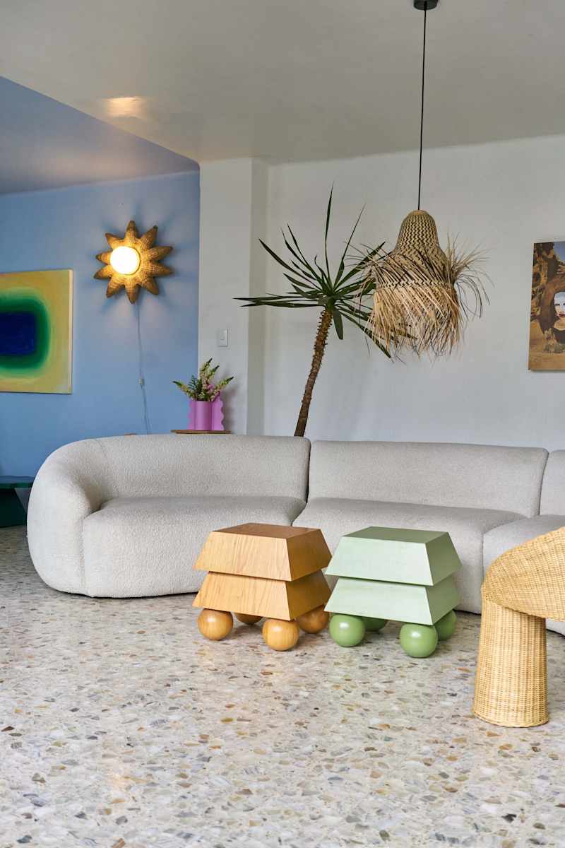 Cozy living room featuring a curved beige sofa, colorful side tables, a hanging light, and a potted plant.